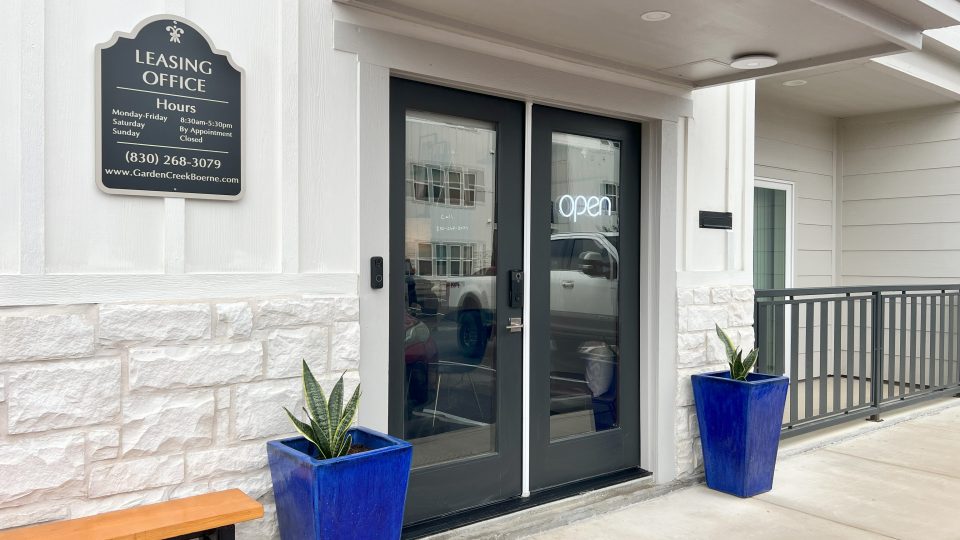 the entrance to a building with two blue potted plants at The Garden Creek Apartments
